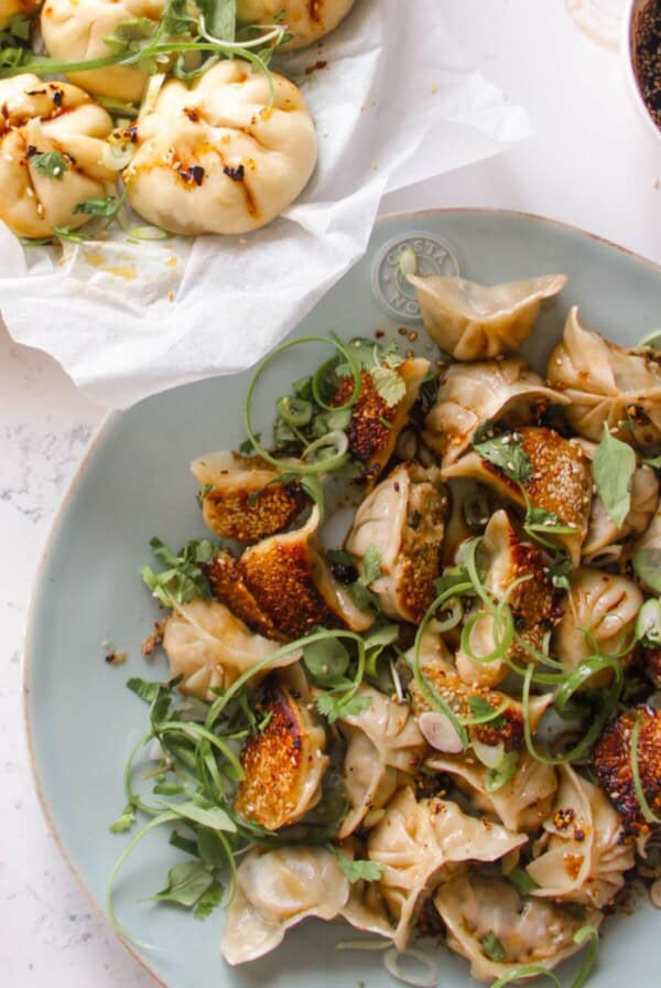 Chicken potstickers on a large blue plate with sauce and steamed buns on the side.