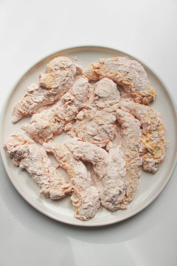 Flour coated chicken on a white plate.