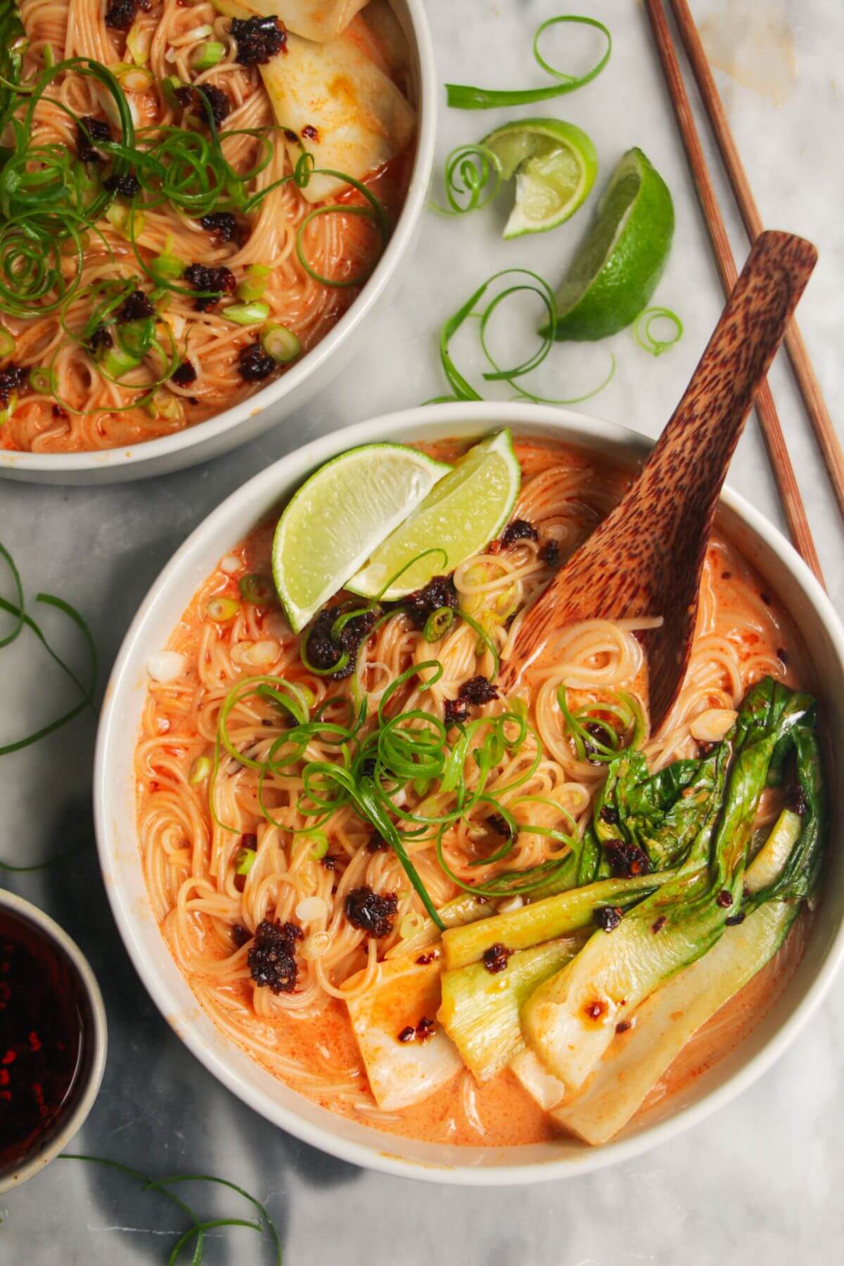 Two bowls of coconut gochujang noodles with lime and spring onion on top.