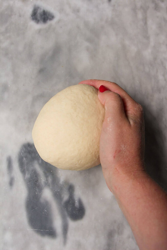 Hand holding ball of dumpling dough on a grey marble background.