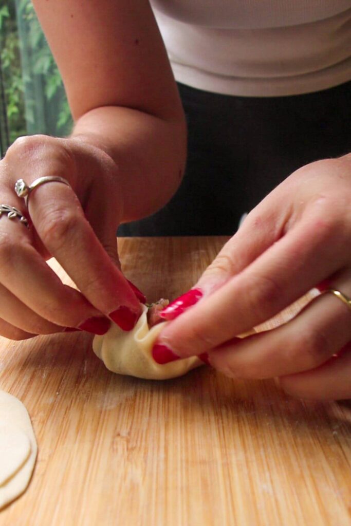 Hands folding dumpling on a wooden board.