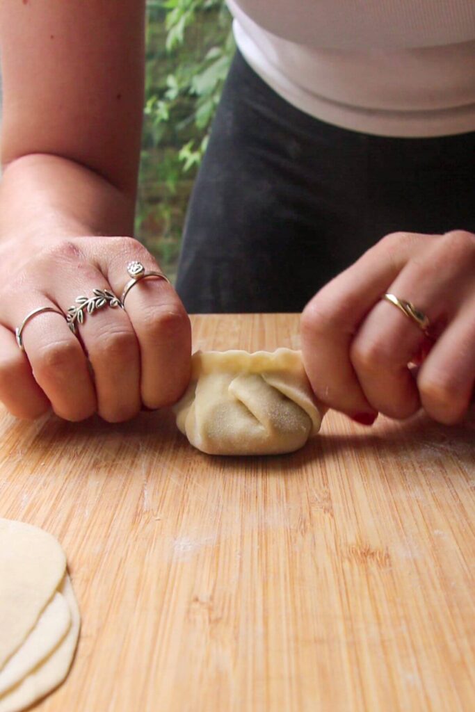 Hands folding dumpling on a wooden board.