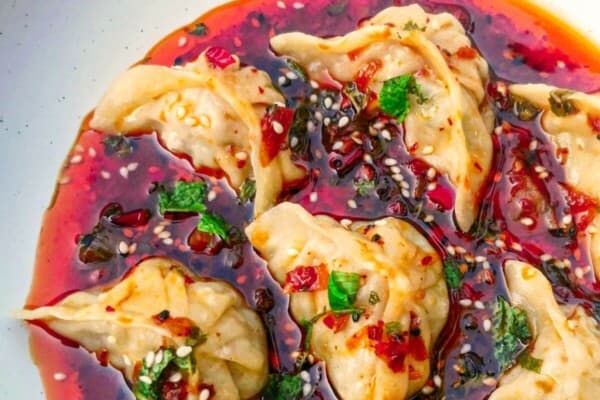 Dumplings in a bowl with red dipping sauce.