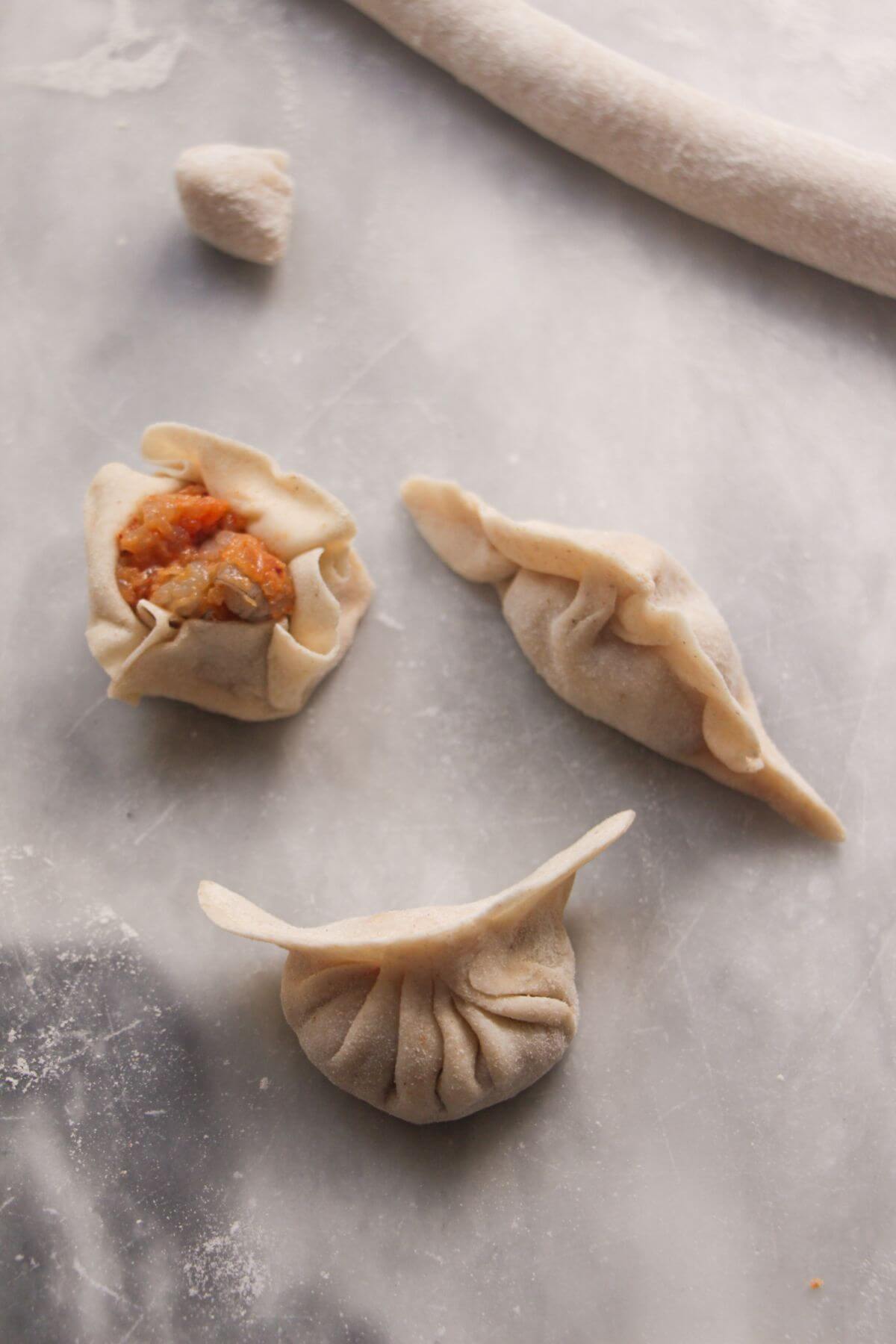 Three different styles of folded dumplings on a marble background.