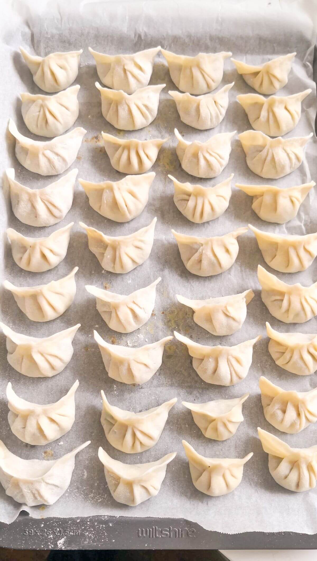 Dumplings laid out on a lined baking tray.