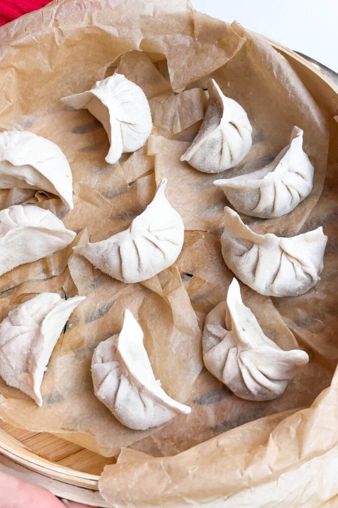 Pleated dumplings in a baking paper lined bamboo steamer.