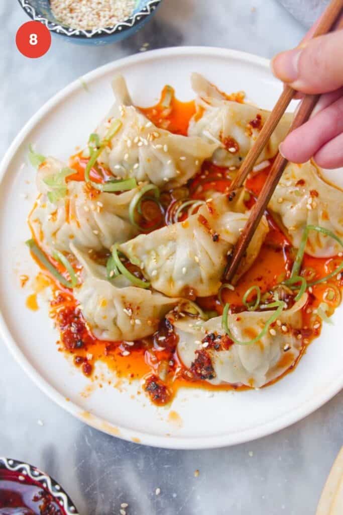 Dumplings on a bed of chili oil, one being picked up with chopsticks.