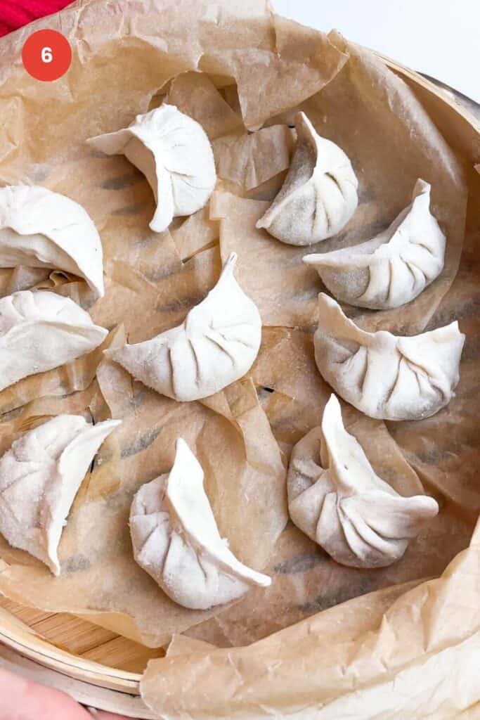 Half moon dumplings in a lined bamboo steamer.