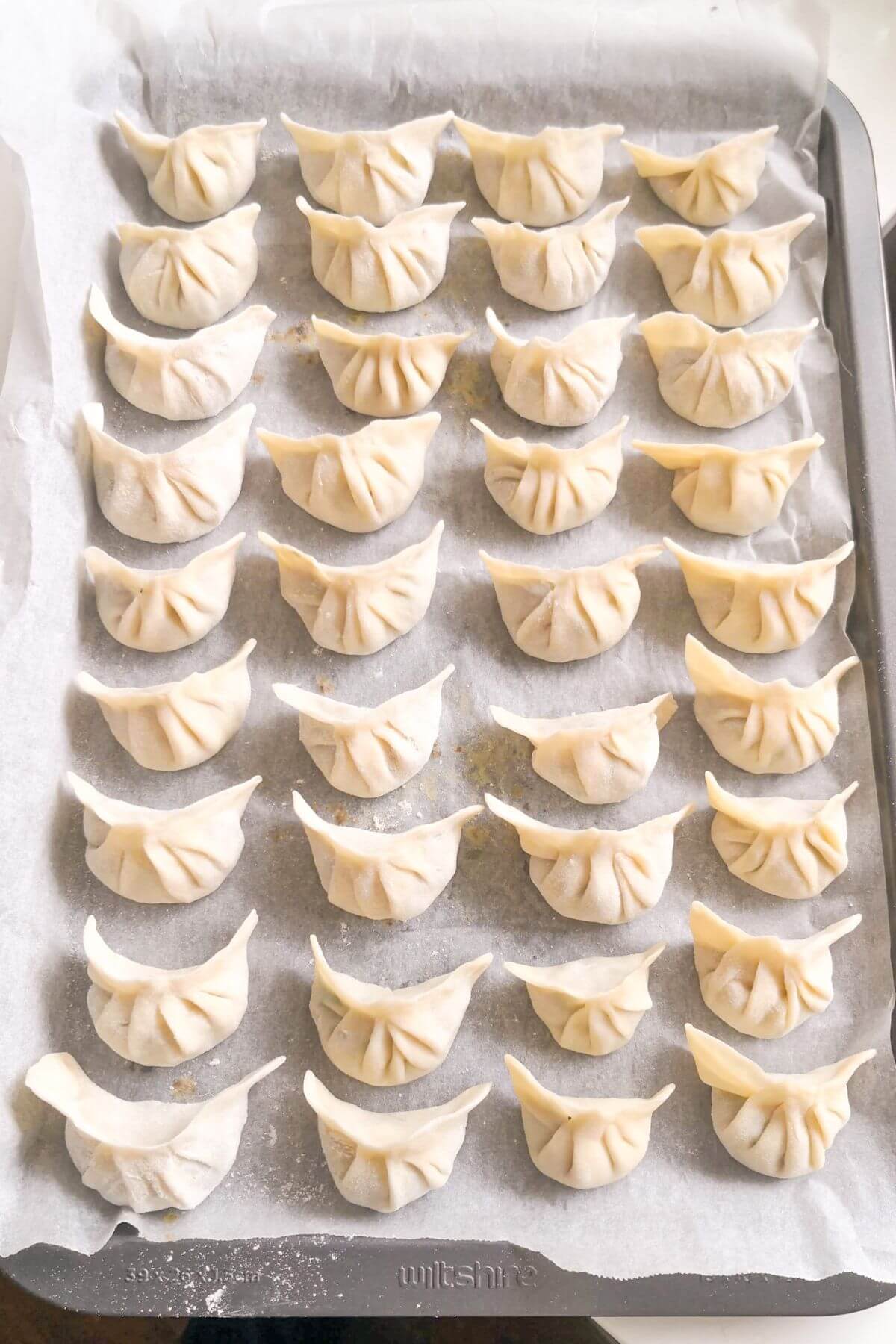 Dumplings laid out on a lined baking tray.