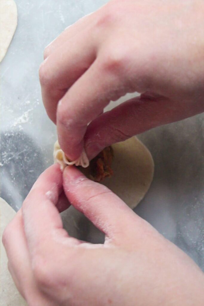Hands folding a dumpling.