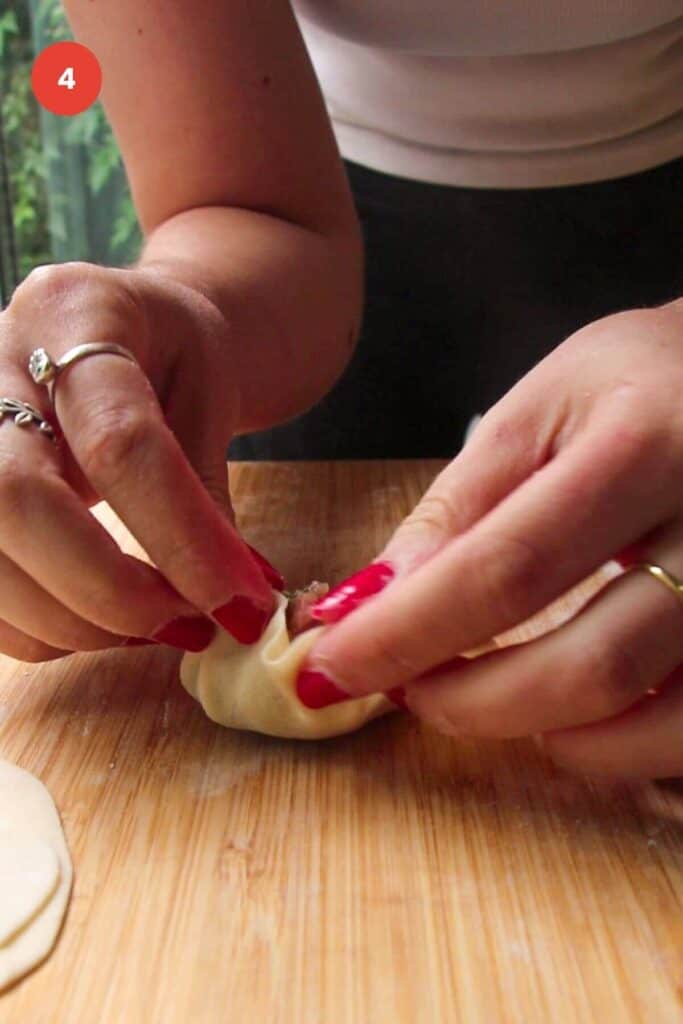 Hands folding dumpling on wooden board.