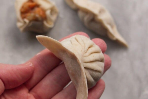 Hand holding a pleated dumpling with two other dumplings in the background.