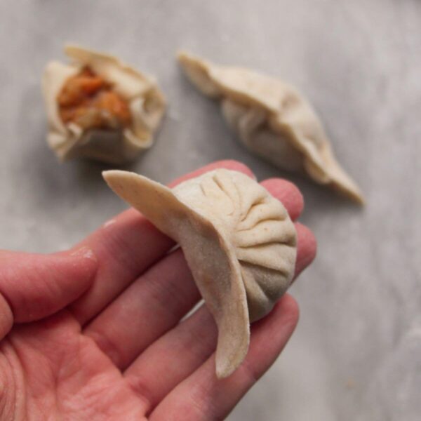 Hand holding a pleated dumpling with two other dumplings in the background.
