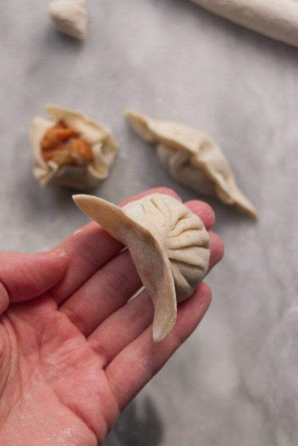 Hand holding a pleated dumpling with two other dumplings in the background.