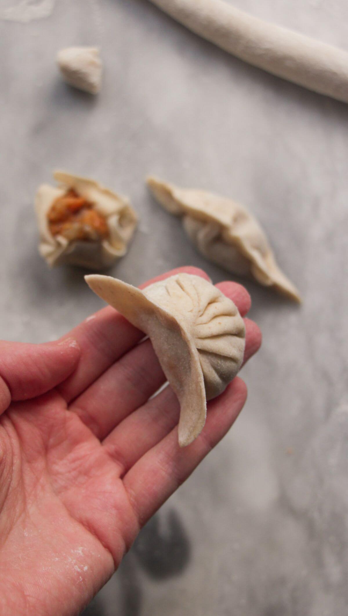 Hand holding a pleated dumpling with two other dumplings in the background.