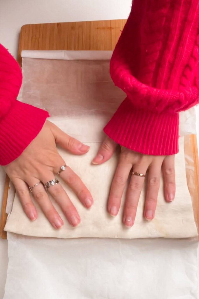 Hands folding over pastry on a wooden board.