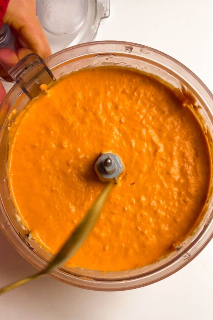 Blitzed red pepper hummus in the bowl of a food processor.