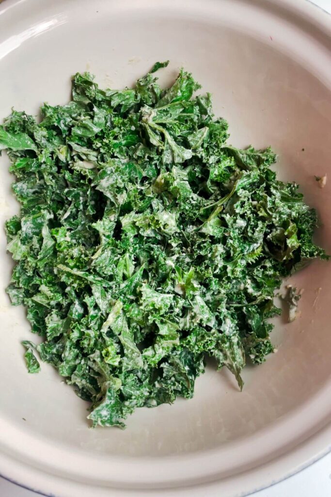 Tahini dressing massaged into kale in a white bowl.