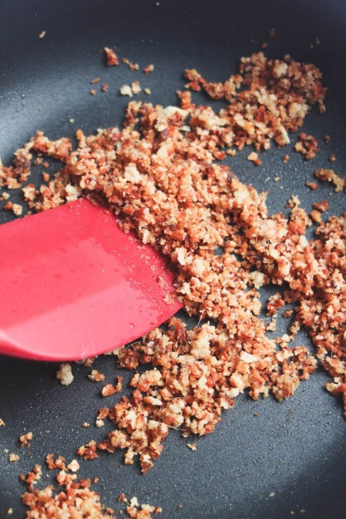 Spatula stirring breadcrumbs through olive oil and anchovies.