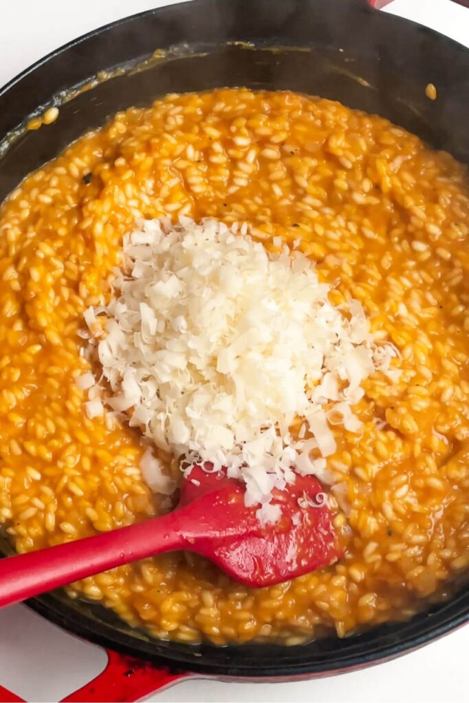 Grated parmesan cheese added to butternut squash risotto in a pan.