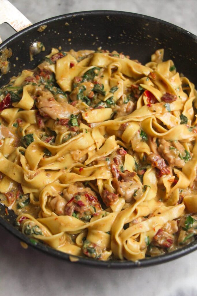 Fettuccine tossed with sunried tomatoes, spinach and chicken in small pan.