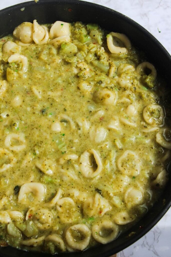 Pasta stirred through broccoli sauce in a large pan.