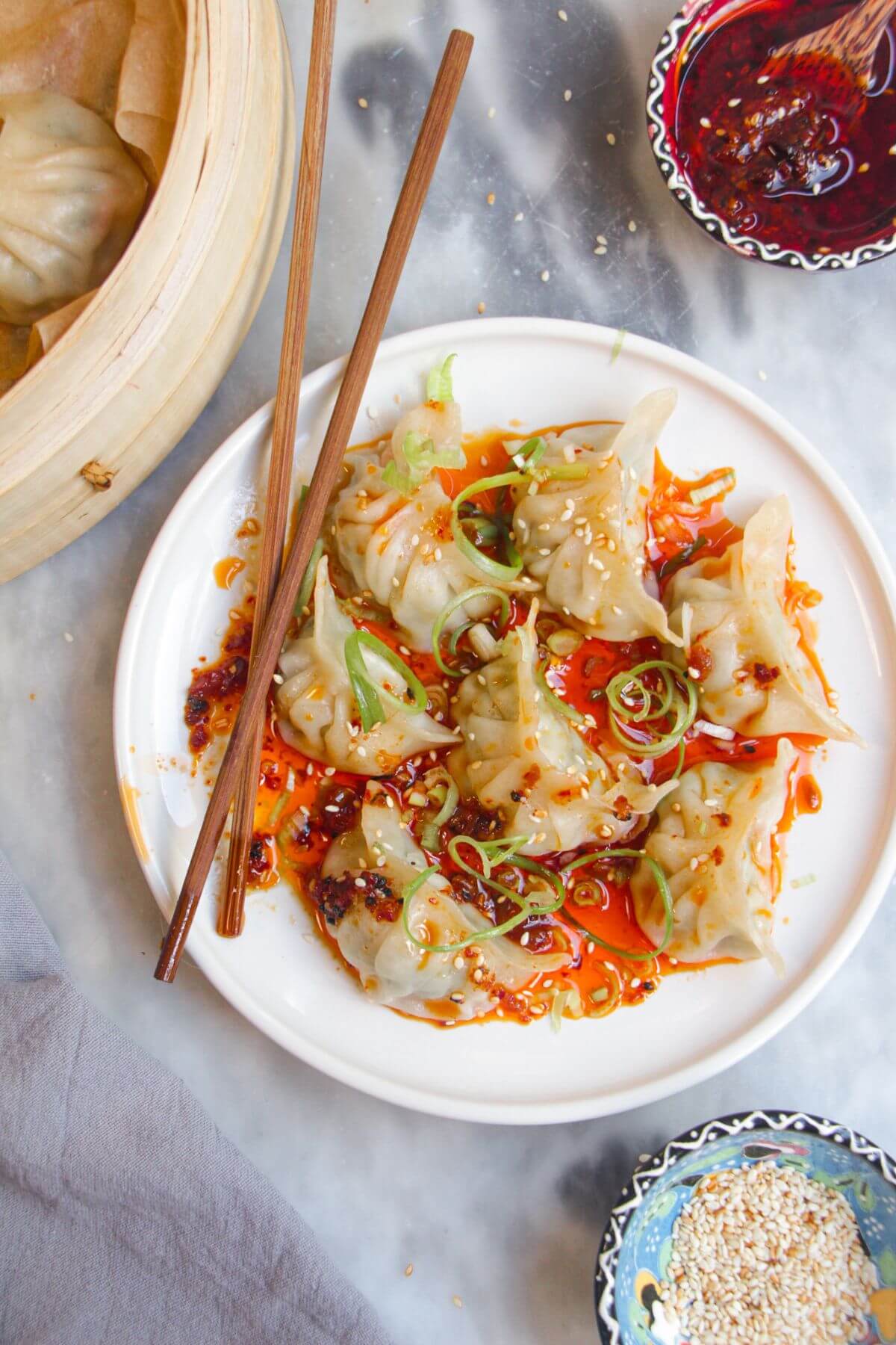 Steamed dumplings on a small white plate, drizzled with chilli oil.