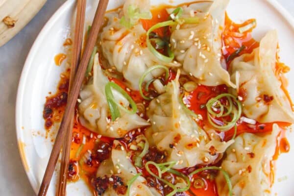 Steamed dumplings on a small white plate, drizzled with chilli oil.