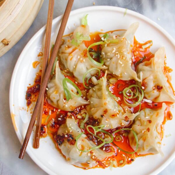 Steamed dumplings on a small white plate, drizzled with chilli oil.