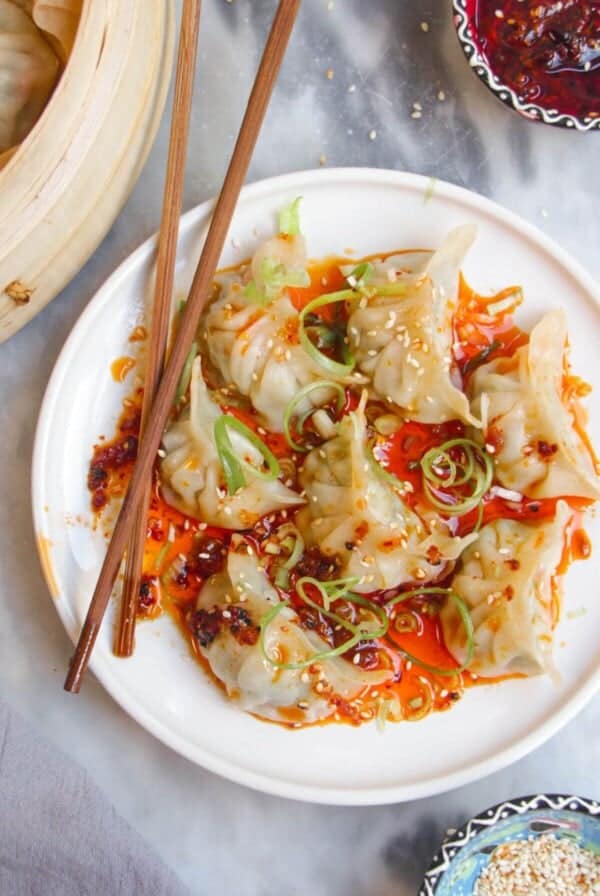 Steamed dumplings on a small white plate, drizzled with chilli oil.