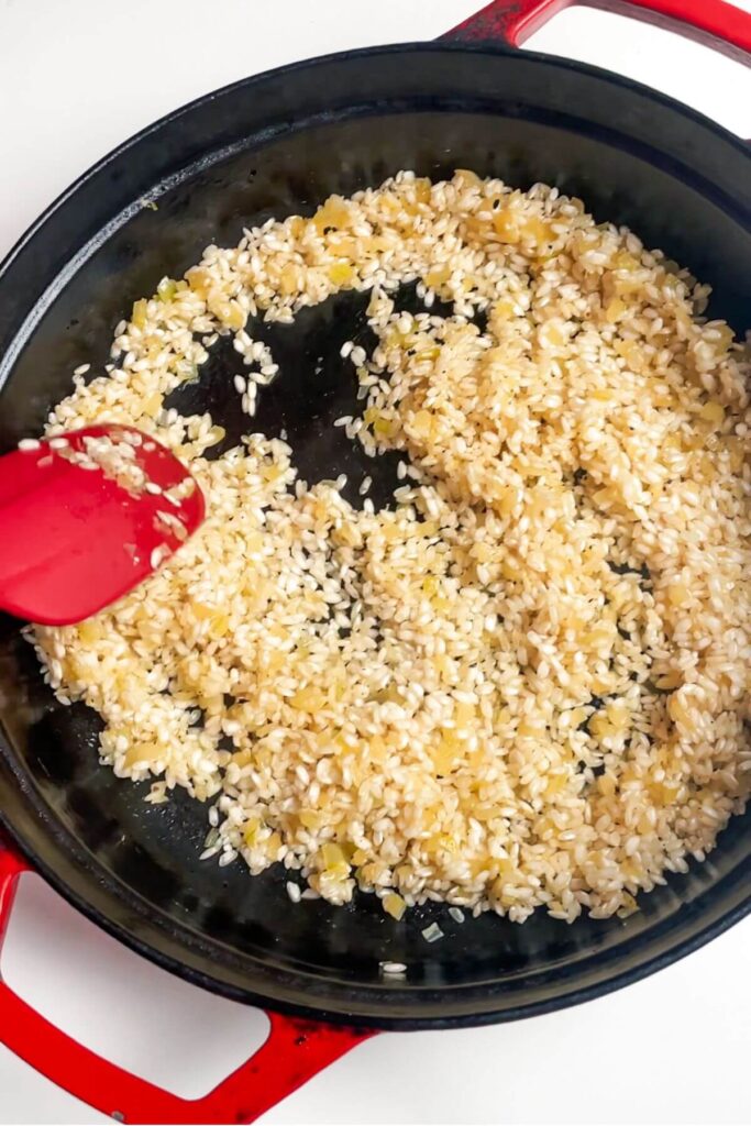 Rice stirred through onion and garli in a pan.