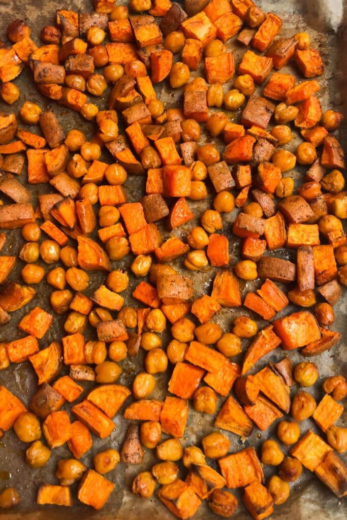 Roasted sweet potatoes and chickpeas on a lined oven tray.