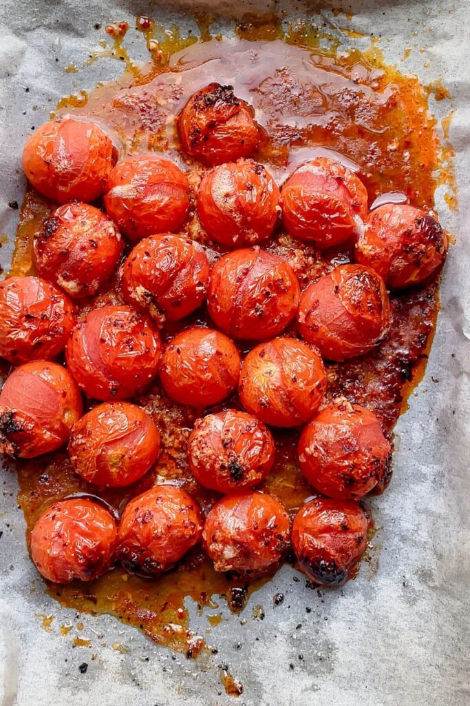 Roasted cherry tomatoes on a lined oven tray.