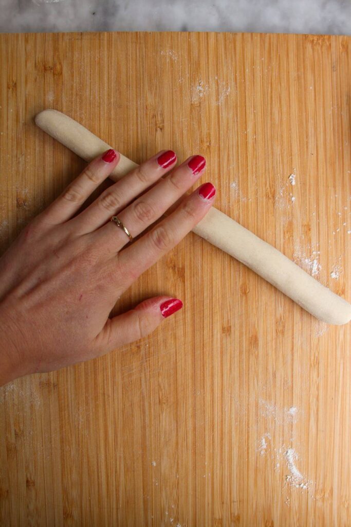 Hand rolling dumpling dough into a long rope on a wooden board.