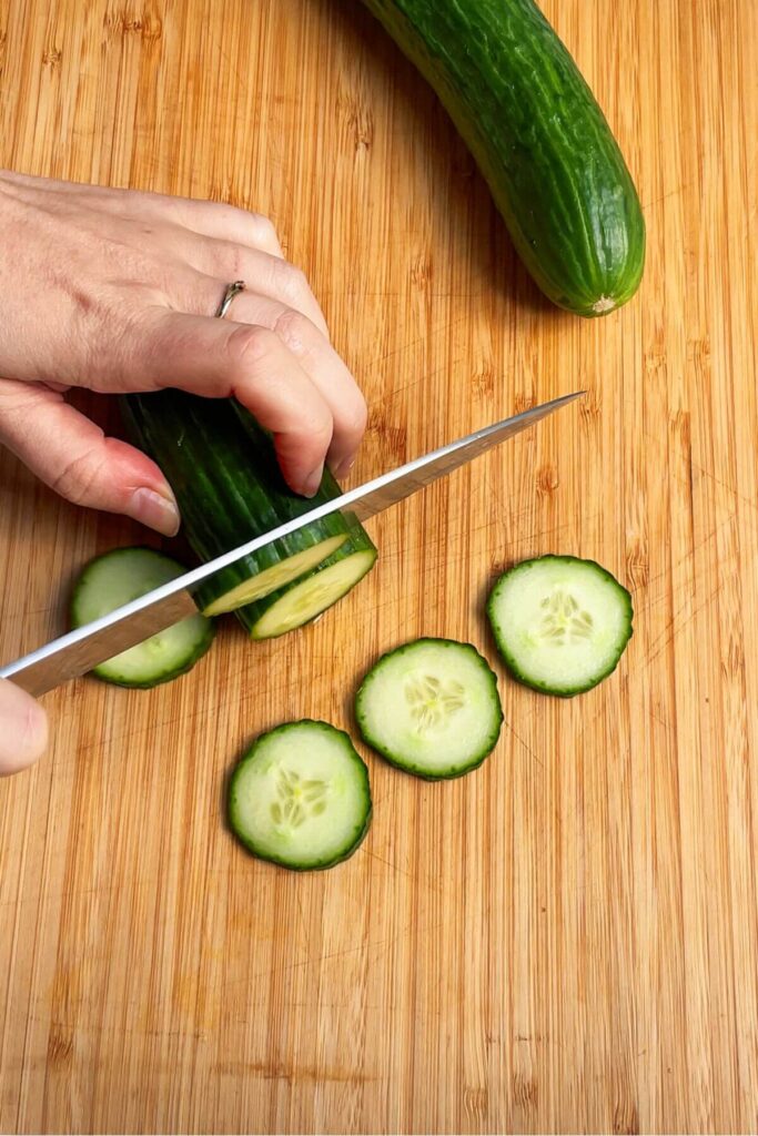 Slicing cucumber on a wooden board.