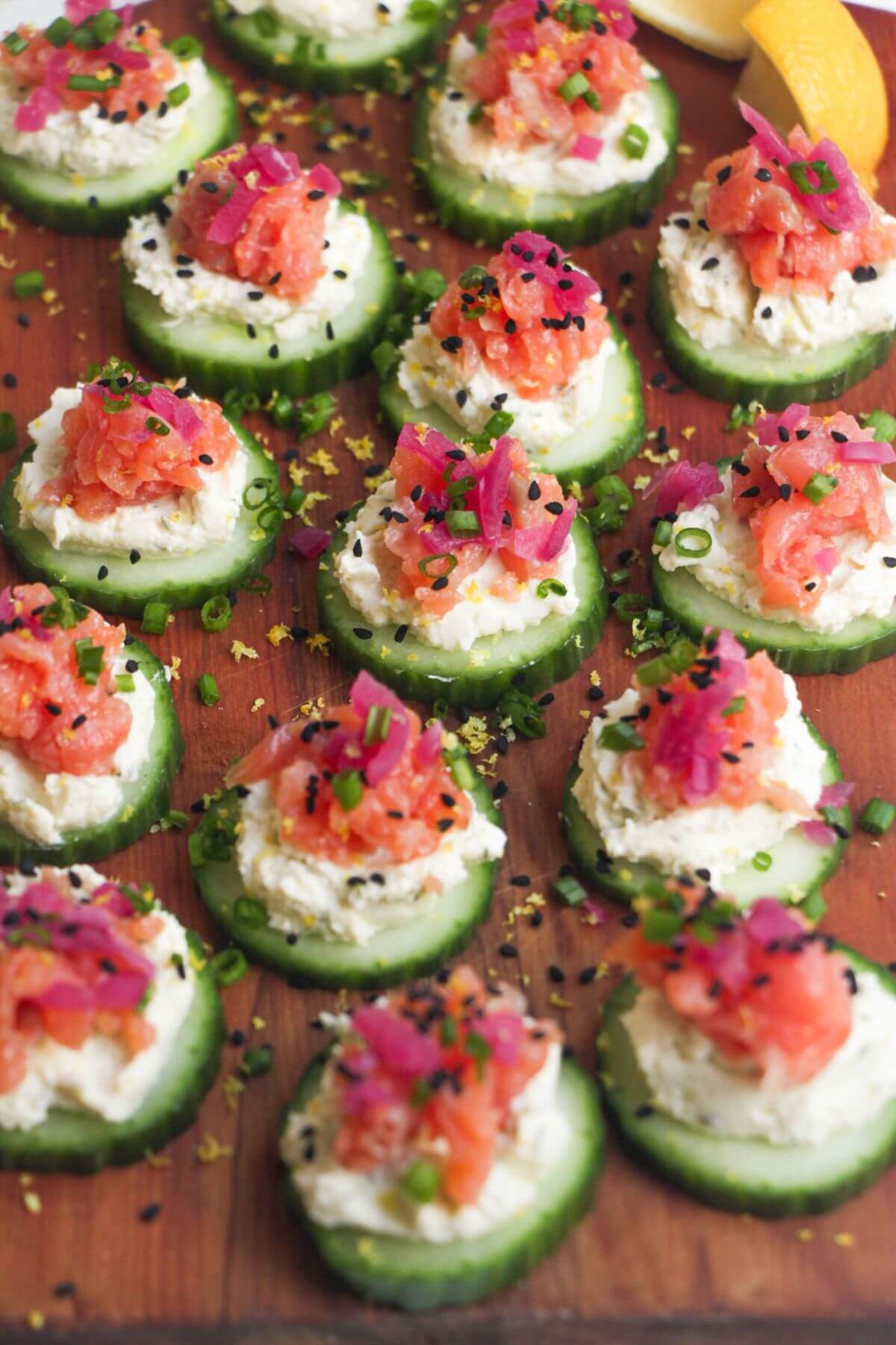 Smoked salmon cucumber bites topped with lemon zest and chives on a wooden board.