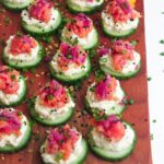 Smoked salmon cucumber bites topped with lemon zest and chives on a wooden board.