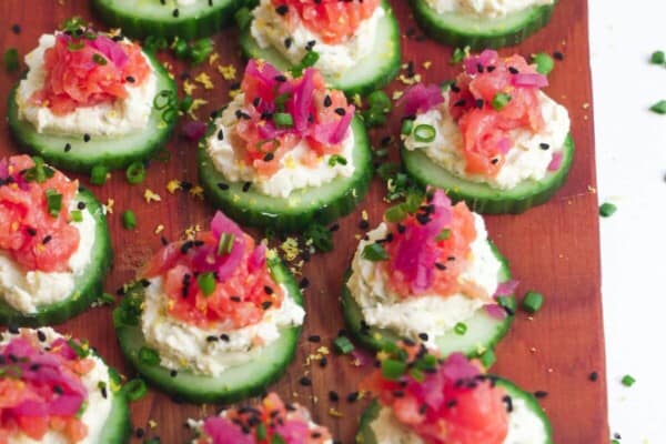 Smoked salmon cucumber bites topped with lemon zest and chives on a wooden board.