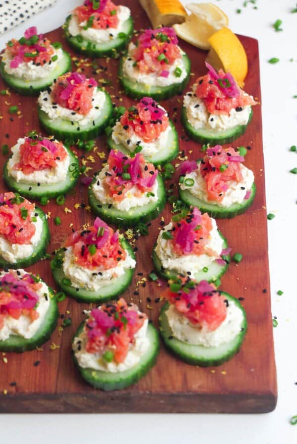 Smoked salmon cucumber bites topped with lemon zest and chives on a wooden board.