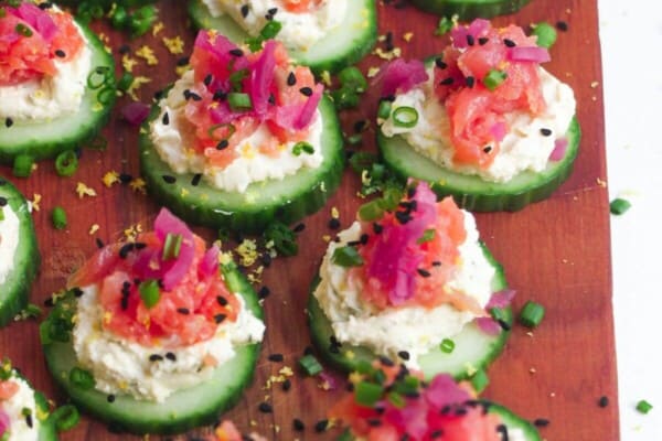 Smoked salmon cucumber bites topped with lemon zest and chives on a wooden board.