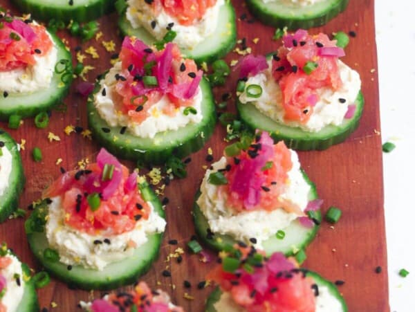 Smoked salmon cucumber bites topped with lemon zest and chives on a wooden board.