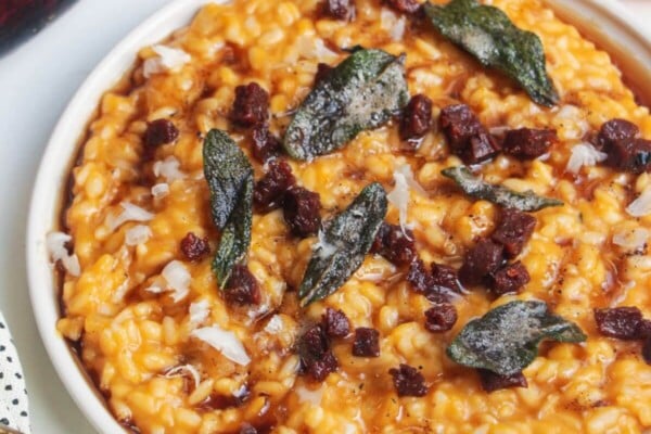 Butternut squash risotto on a small white plate, topped with sage brown butter and chorizo.