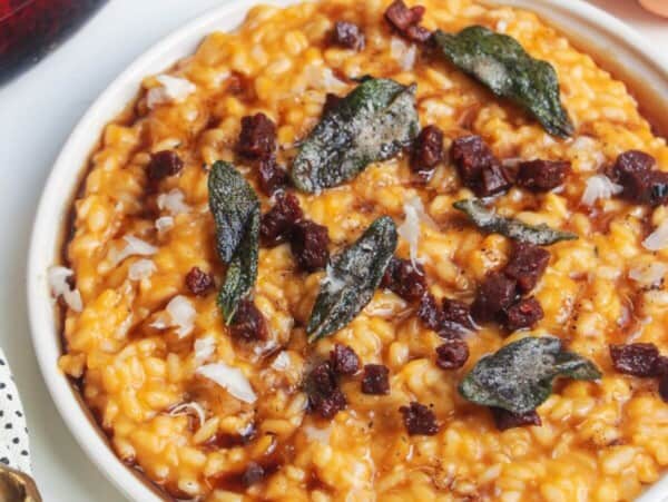 Butternut squash risotto on a small white plate, topped with sage brown butter and chorizo.