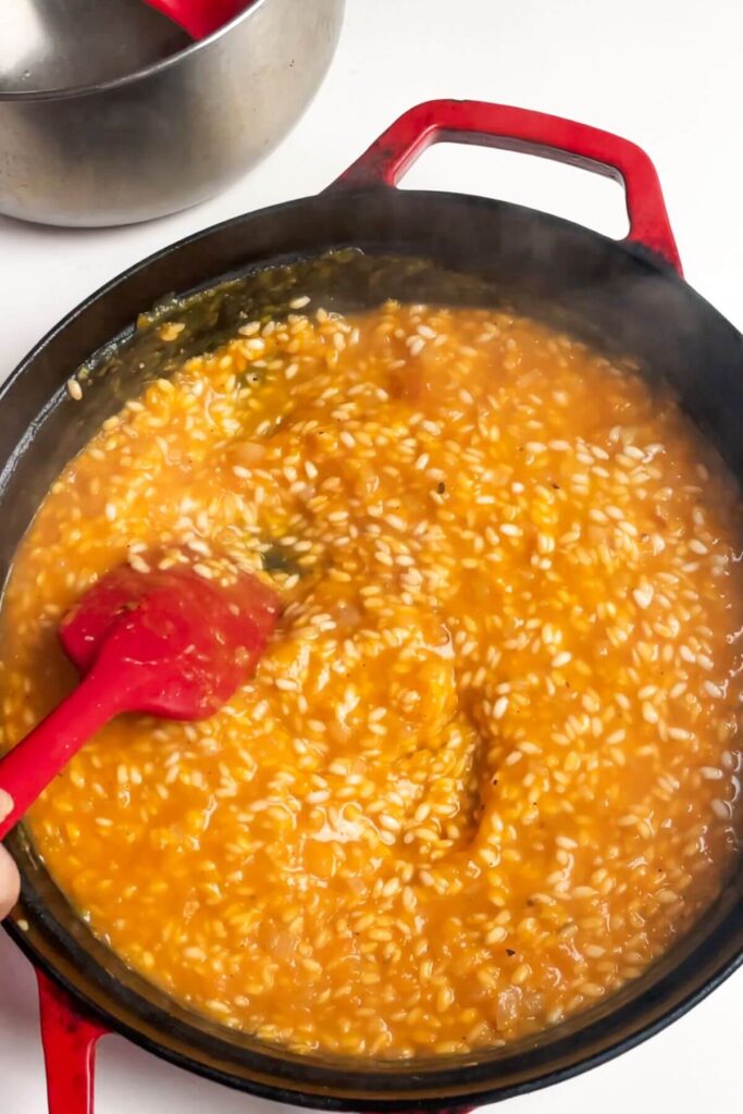 Red spatula stirring butternut squash risotto in a pan.