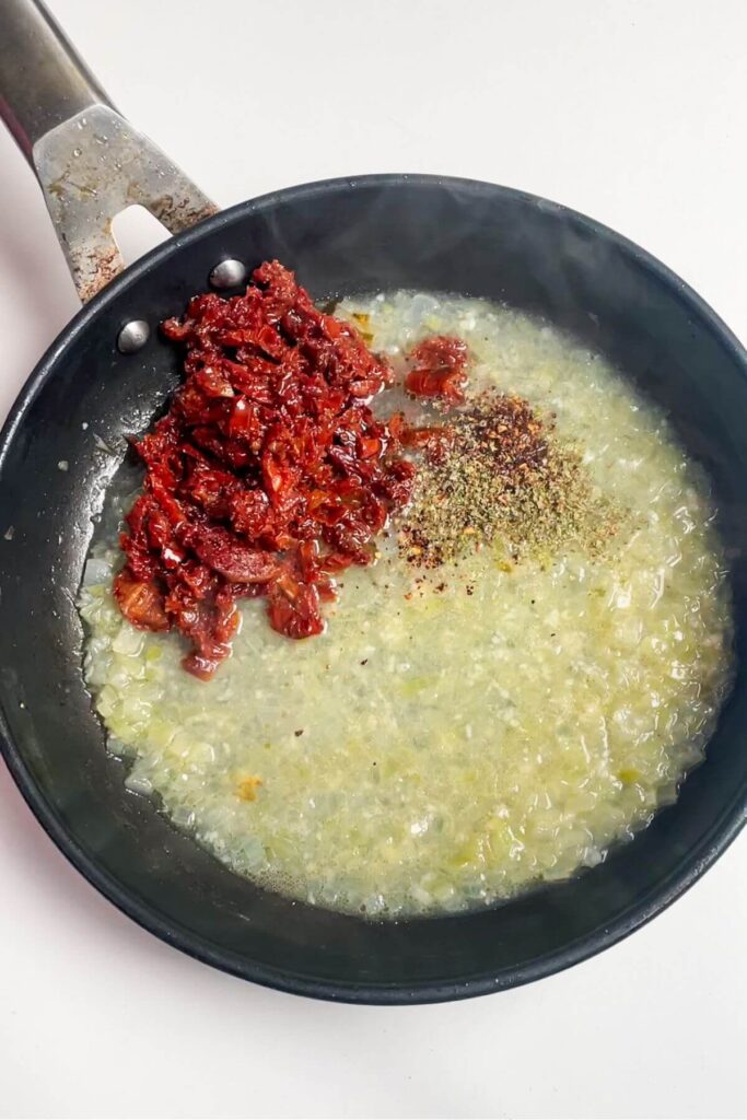 Chopped sundried tomatoes added to onions cooking in a pan.