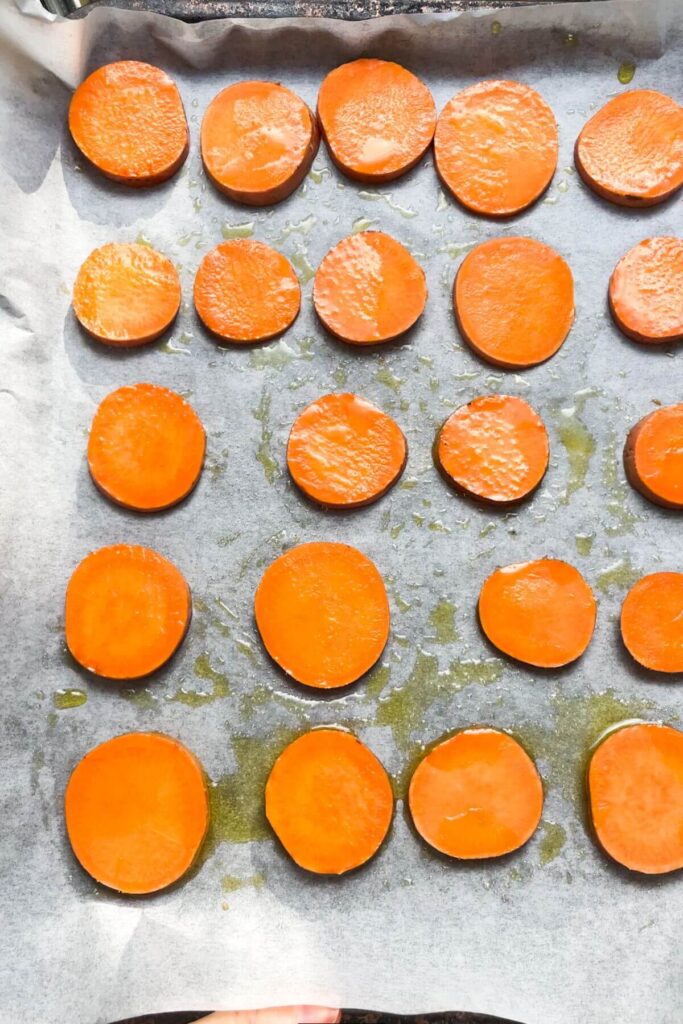 Sweet potato discs on a lined baking tray, drizzled with olive oil.