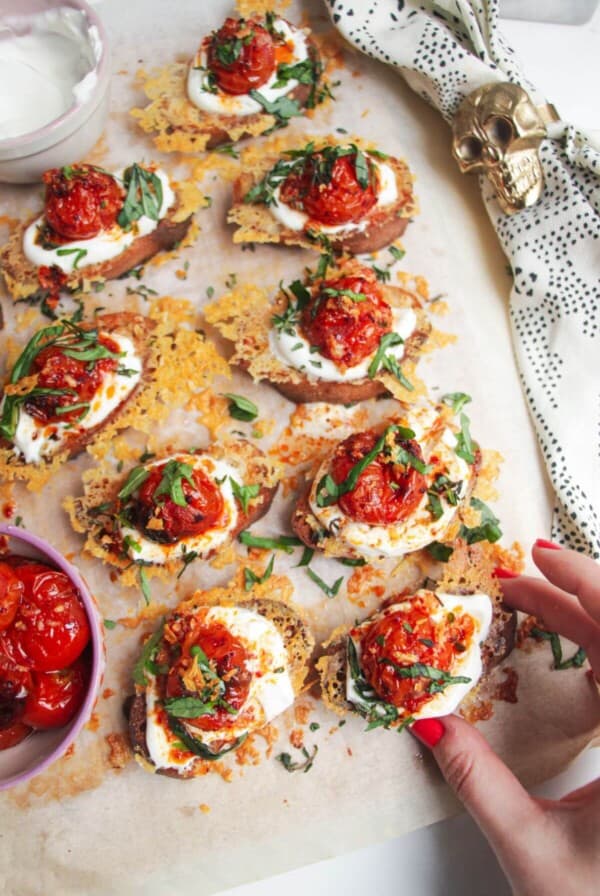 Cheesy crusted roasted tomato crostini on a wooden borad with more tomatoes on the side.