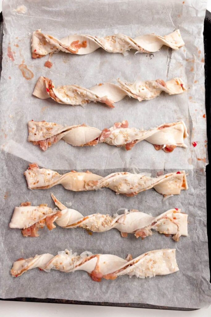 Unbaked bacon cheese twists on a lined oven tray.