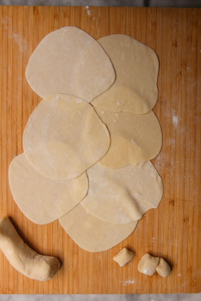 Round dumpling wrappers overlapping on a large wooden board.