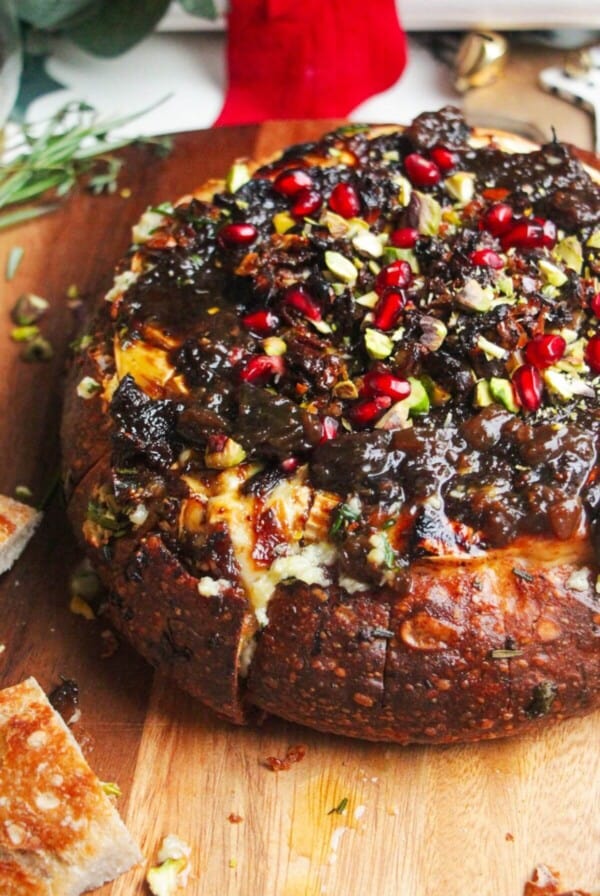 Baked brie in a loaf of bread, topped with fig jam and pomegranate seeds.